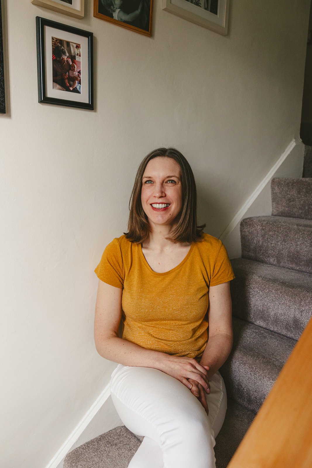 Woman smiling on stairs with framed photos.